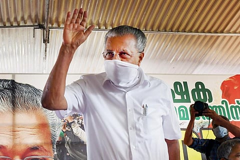 Kerala Chief Minister Pinarayi Vijayan, wearing a white mask, standing and waving 