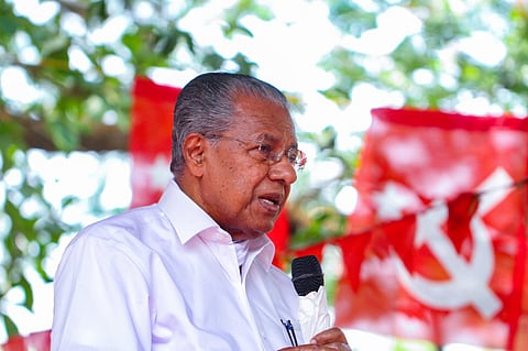 Outgoing chief minister Pinarayi Vijayan speaks through a microphone. CPIM flags in the background 
