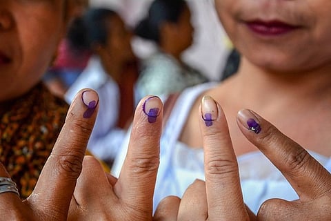 Women hold up their ink-marked fingers after casting their votes, showing the purple indelible ink on their fingertips. The image captures a close-up view, with the background slightly blurred to focus on the voters' hands.