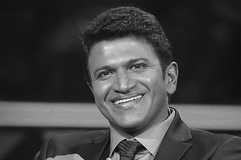 Black and white image of Puneeth Rajkumar looking into the camera, smiling