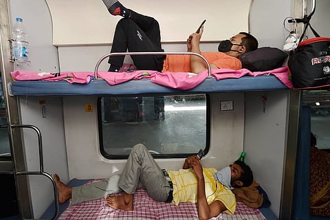 Two passengers lying down on the berths in a train using their mobile phones