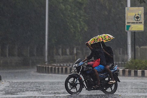A couple travelling on a two-wheeler with an umbrella amid heavy rains