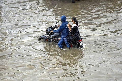 Representative image of two people riding a scooter through flooded streets