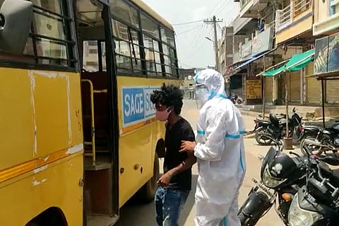 A police man wearing a PPE kit escorting a youngster into a bus