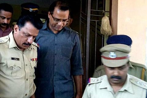 Robin Vadakkumchery (middle) along with police officers. Robin is smiling lightly 