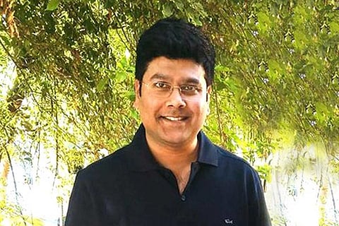 Sabareesan stands wearing a black shirt with greenery behind