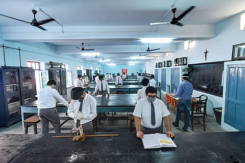 Students standing at desks in a laboratory wearing masks and maintaining distance 