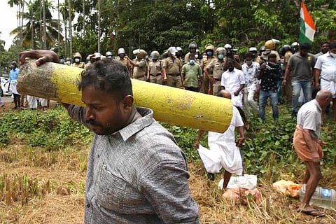 A man carrying a survey stone as protesters stand behind police officials