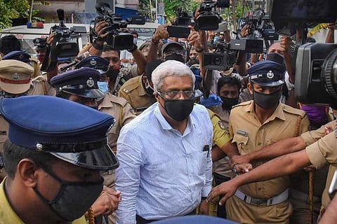 Suspended Kerala IAS officer wearing a mask and surrounded by police officials