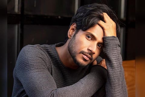 Sundeep Kishan is seen wearing a full sleeved gray tee in the image while striking a pose.