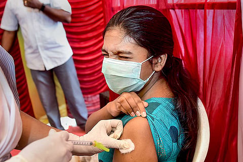 A girl, wearing a mask, being administered the vaccine dose by a health worker. 