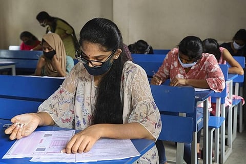 TS Inter Results 2021: Students sitting at individual benches while wearing masks, writing an exam