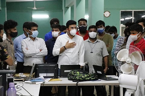Tejasvi Surya in a white shirt and white mask with his hand on his chest speaking with BBMP War Room staff members