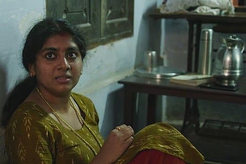 Nimisha Sajayan wearing a green kurta and sitting on the floor in The Great Indian Kitchen