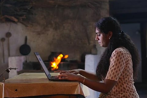 Nimisha Sajayan in The Great Indian Kitchen, she is sitting on a chair and looking at her laptop on the table