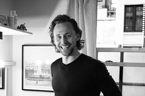 A black and white photo of Tom Hiddleston standing in a kitchen and laughing