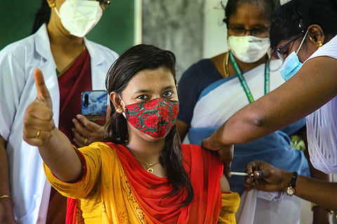 A woman wearing a mask gives the thumbs up as she gets vaccinated by a nurse in Kanniyakumari with other staff behind her