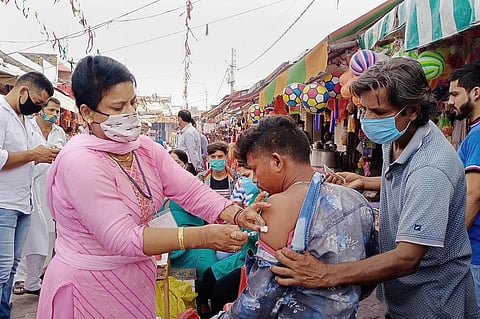 A health worker in Jammu vaccinates a young man who exposes his arm while another person holds down his shirt 