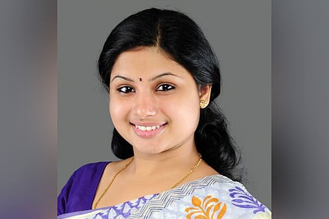 Congress leader Veena S Nair in white and purple saree looking into the camera and smiling