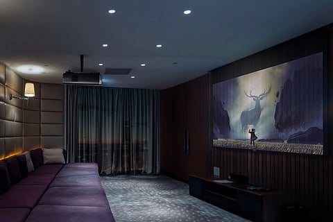 Image of sofa at one end of a room with a movie being projected on the wall opposite 