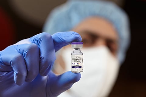 A health worker holding up a small bottle labelled ZycovD