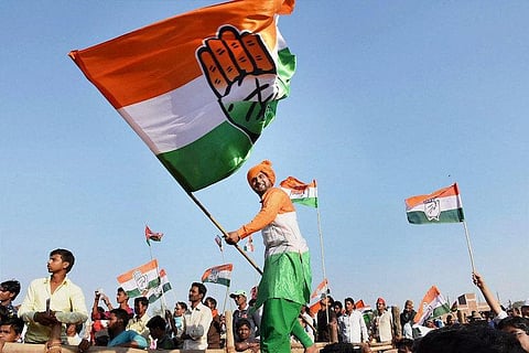 A man wearing tricolour robes waves a big Congress flag at a Congress rally