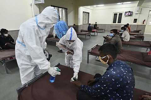 A man gets his spo2 checked with an oximeter as two healthcare workers in ppe stand before him 