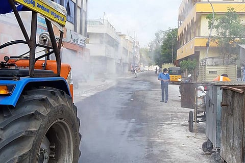A street in Chennai being disinfected as a man wearing mask walks by. 