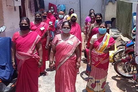 Domestic Workers in pink saree standing in three rows, wearing masks 