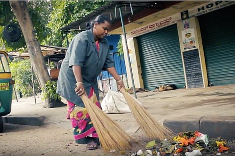 A Pourakarmika sweeping the road