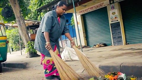 A woman waste management worker sweeping a street in uniform.