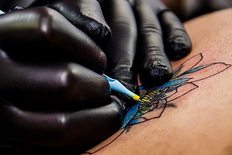 A close up of a tattoo artist wearing black gloves drawing a tattoo on skin 