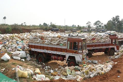 Trucks filled with plastic and other waste bags parked at a dump yard surrounded by heaps of garbage in Tamil Nadu.