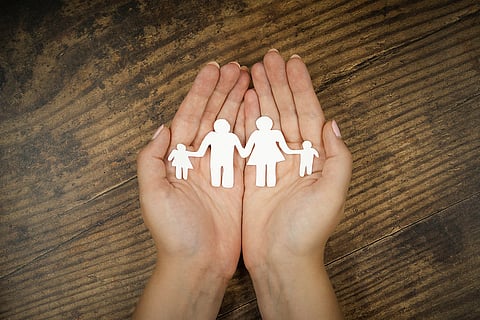 The concept of parenting and family, depicted using a family-shaped paper cut out being held in hands over a wooden background.