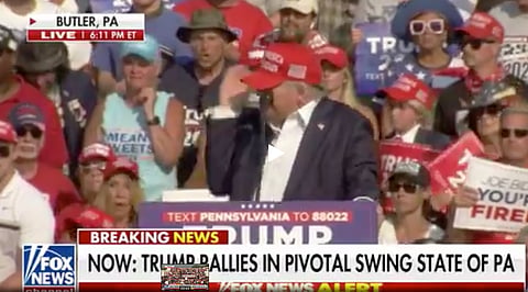 A spectator behind former president Donald Trump reacts with horror as Trump clutches at his ear, having just apparently taken a shot. A person said to the shooter, has now been killed. Trump says he is 'fine.'