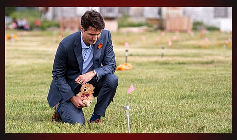 Prime Minister Justin Trudeau in a cemetery near a residential school holding a teddy bear