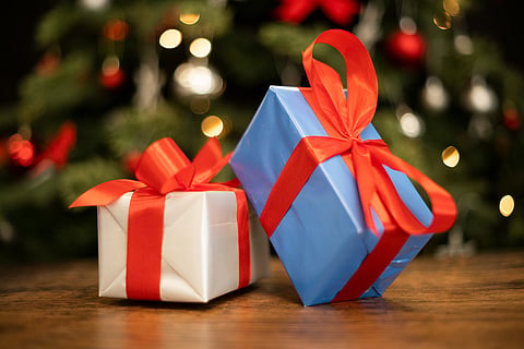 Photo of a couple of gift wrapped Christmas presents with a beautiful Christmas tree in the background. 