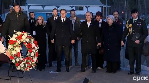 A screenshot of Mark Carney, Pierre Poilevre, Mary Simon, David Eby, and Wendy Cocchia holding hands at the Tumbler Ridge vigil on Friday. 