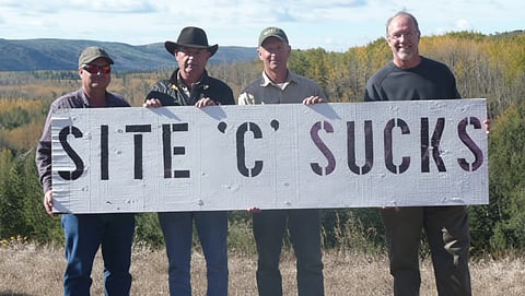 John Horgan (far right) and fellow opponents of the Site C dam hold a protest sign in the Peace River region. (File photo)