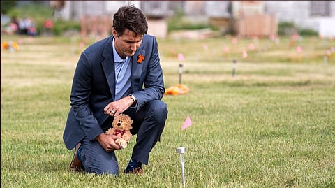 Prime Minister Justin Trudeau in a cemetery near a residential school holding a teddy bear