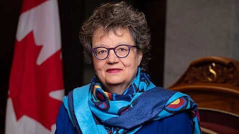 Senator Paula Simons posing in front of a Canadian flag.