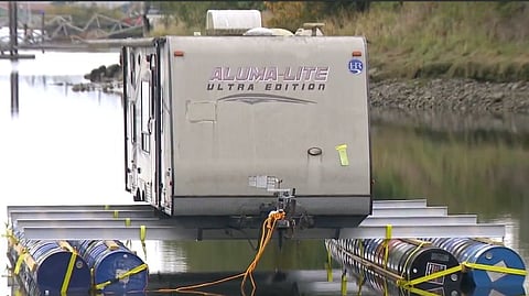An Aluma-Lite Ultra Edition travel trailer sits on steel beams and barrel pontoons on the Nicomekl River in South Surrey.