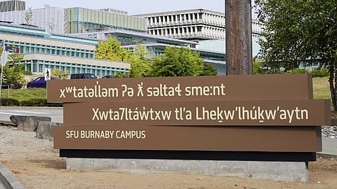 The new roadside sign at Simon Fraser University's Burnaby campus. The top two planks carry the gifted hən̓q̓əmin̓əm̓ and Sḵwx̱wú7mesh names. The bottom plank still reads "SFU BURNABY CAMPUS."