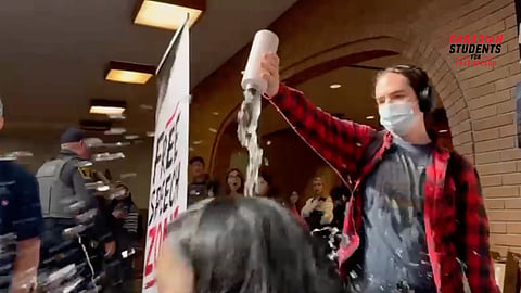 A masked individual pours water on the head of Dr. Tom Flanagan at a residential school campus discussion